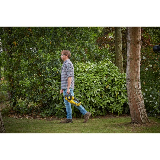 STANLEY SFMCHT855M1 hedge trimmer held by person walking outdoors, product in landscape use context.