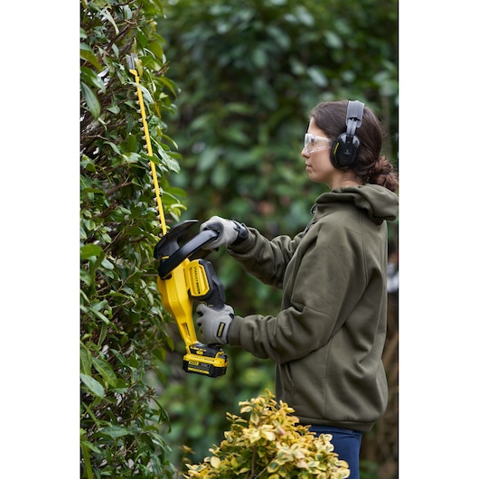 STANLEY SFMCHT855M1 cordless hedge trimmer in use outdoors, yellow and black design, side angle.