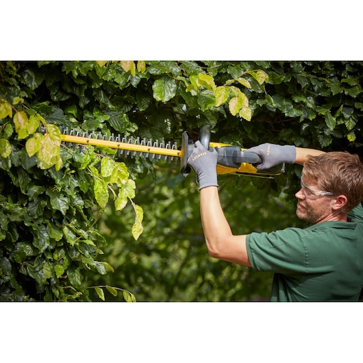 STANLEY SFMCHTB866B hedge trimmer in use trimming green foliage outdoors, close-up side angle.
