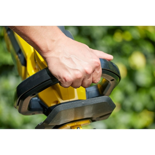 Close-up photo of a hand gripping the front handle of a STANLEY SFMCHTB866B hedge trimmer outdoors.
