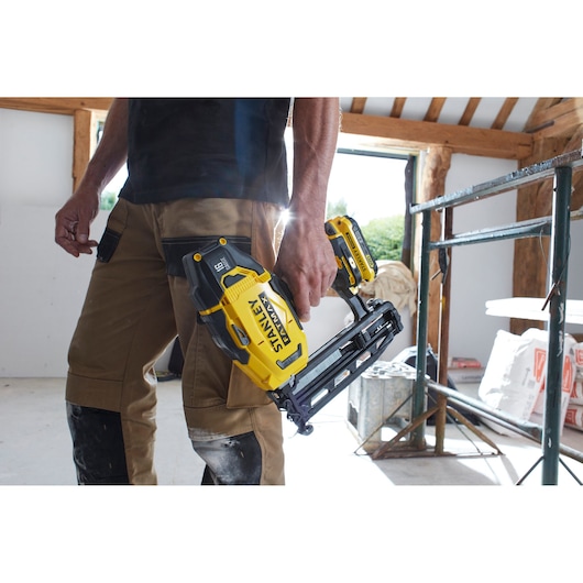 STANLEY SFMCN616D2K cordless nailer held by person in work pants at construction site.