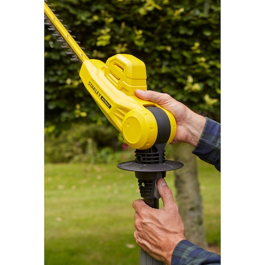 Photo of STANLEY SFMCPH845M1 yellow cordless hedge trimmer being held outdoors in a garden.
