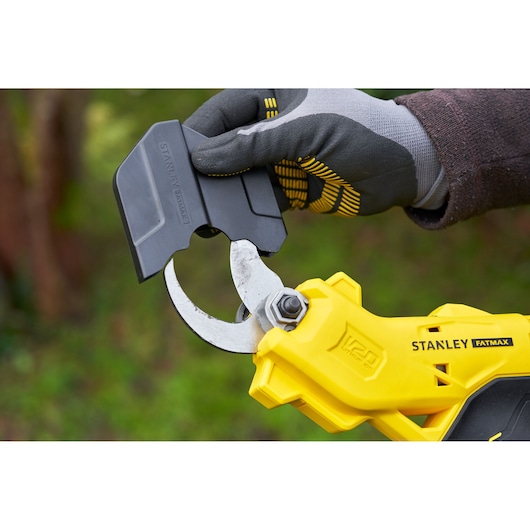 Photo of STANLEY SFMCPP32B garden pruner in yellow, close-up of gloved hand placing black blade cover outdoors.