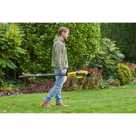 STANLEY SFMCPP632D1 pole pruner held by person outdoors, yellow and black tool in garden setting.