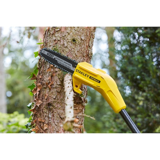 Photo of STANLEY SFMCPS620M1 pole saw cutting a tree branch, showing yellow body and black saw blade outdoors.