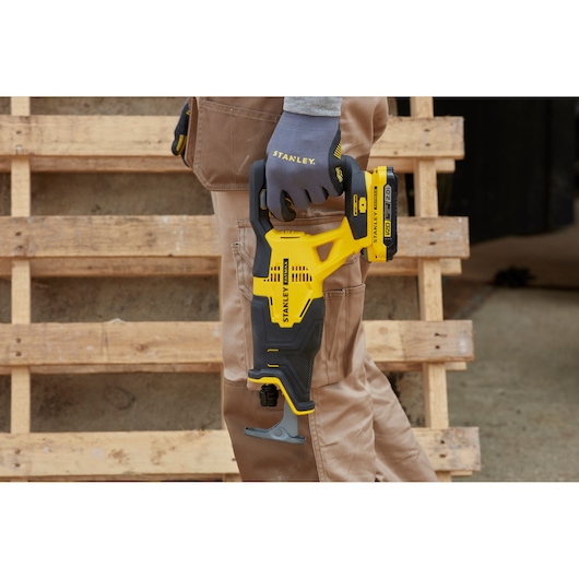 STANLEY SFMCS300D2K cordless reciprocating saw held by gloved hand, yellow and black design, outdoor setting.
