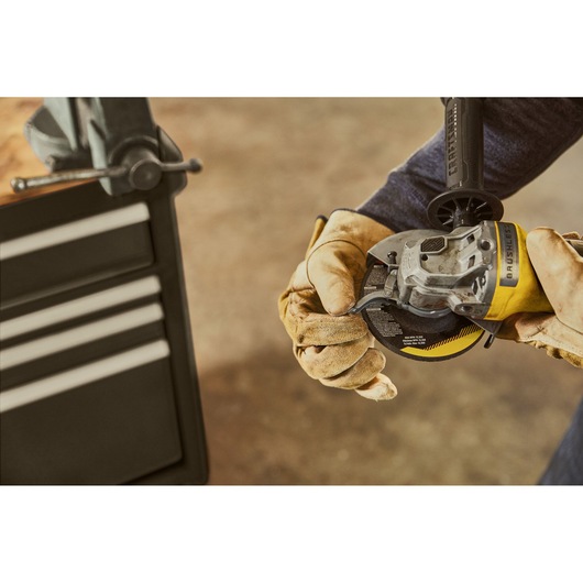 STANLEY SFMCS310B cordless angle grinder held by gloved hands near workshop cabinet.