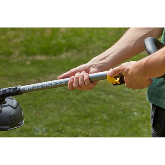 Photo of hands adjusting STANLEY SFMCSTB963B brushless string trimmer shaft outdoors on grass.