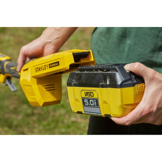 Photo of STANLEY SFMCSTB963B yellow V60 5.0Ah battery being inserted into a STANLEY FATMAX tool outdoors.