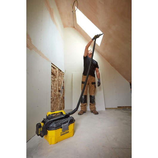 Photo of STANLEY SFMCV002B wet dry vacuum used on a construction site, worker cleaning ceiling with attached hose.