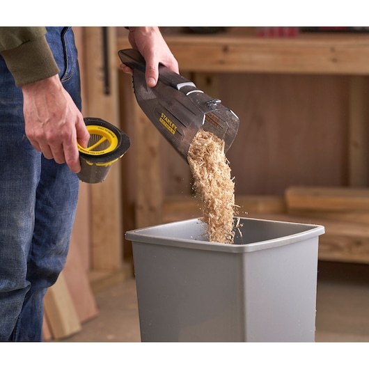 STANLEY SFMCVH001B handheld vacuum being emptied into a bin with filter removed, workshop background.