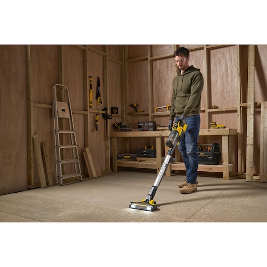 STANLEY SFMCVS001D1 cordless stick vacuum in workshop setting, cleaning sawdust from the floor.