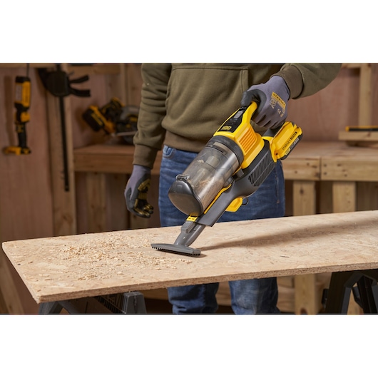 STANLEY SFMCVS001D1 handheld vacuum cleaner being used to clean wood shavings on a workbench, side angle.