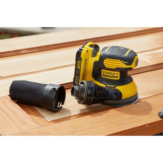 Stanley SFMCW220B cordless sander with dust port, yellow-black, on wooden surface, product photography.