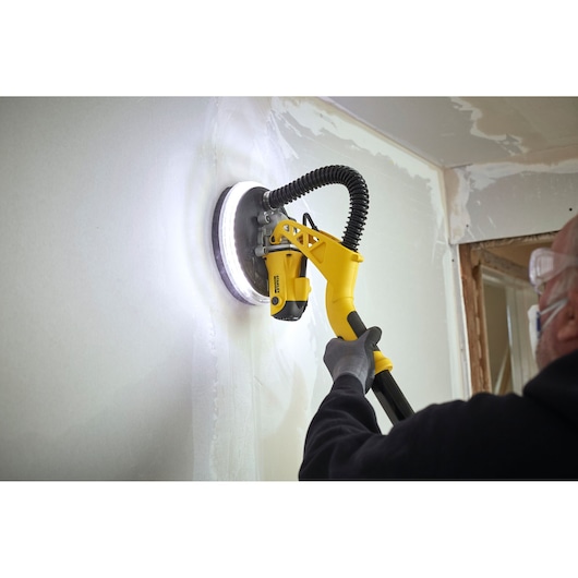 STANLEY SFMEE500S drywall sander in use, yellow handle, sanding white wall, close-up action.