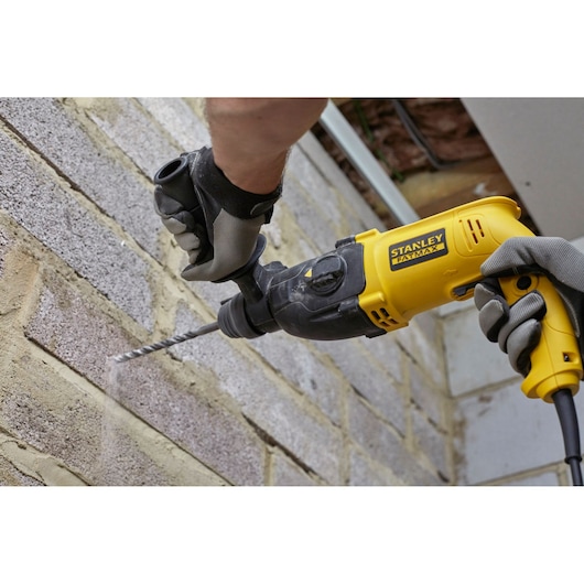 Photo of STANLEY SFMEH200K hammer drill in use on brick wall, yellow and black, product photography.