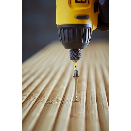 STANLEY STA88558 screwdriver bit in drill driving a screw into grooved wooden surface, close-up photography.