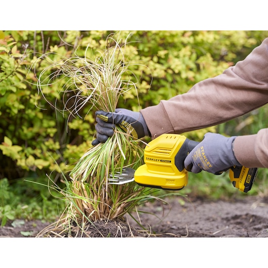 Photo of STANLEY STCSS20D1 grass shear in use, trimming plants in a garden, user wearing gloves.