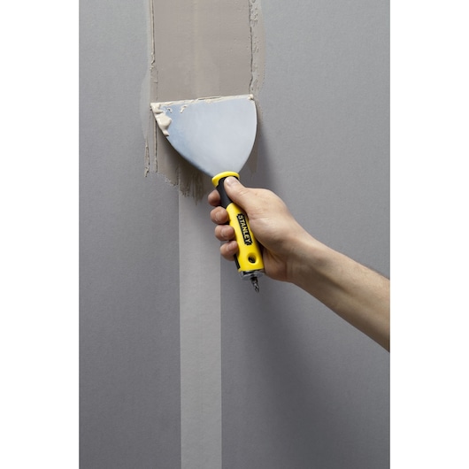 STANLEY STHT0-28034 putty knife with yellow and black handle used to apply filler on a wall.