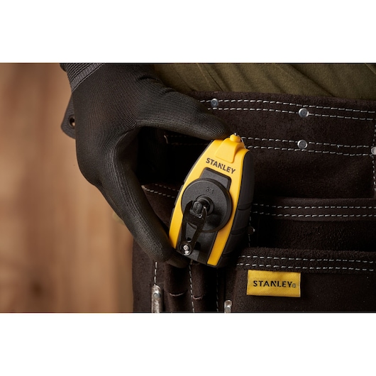 Photo of STANLEY STHT0-47147 chalk line tool, yellow and black, held by gloved hand, clipped to tool belt pouch.