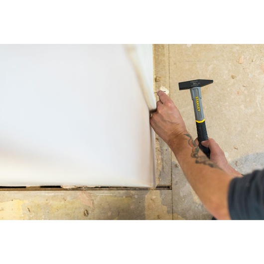 Photo of STANLEY STHT0-51906 hammer in use against drywall, close-up showing tool and user’s hands.
