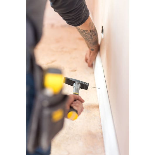 STANLEY STHT0-51908 hammer in use, person nailing baseboard to wall, close-up side photography.