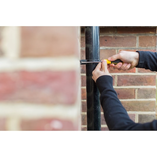 STANLEY STHT0-60280 screwdriver used on outdoor pipe near brick wall, product in hand, side view