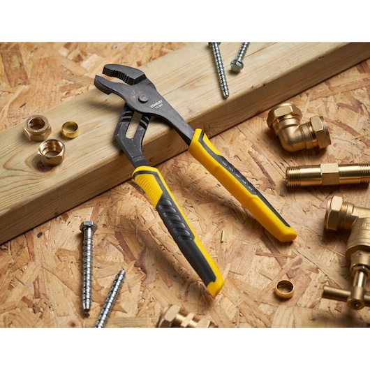STANLEY STHT0-74361 adjustable pliers with yellow and black handles on wood with plumbing fittings and screws.