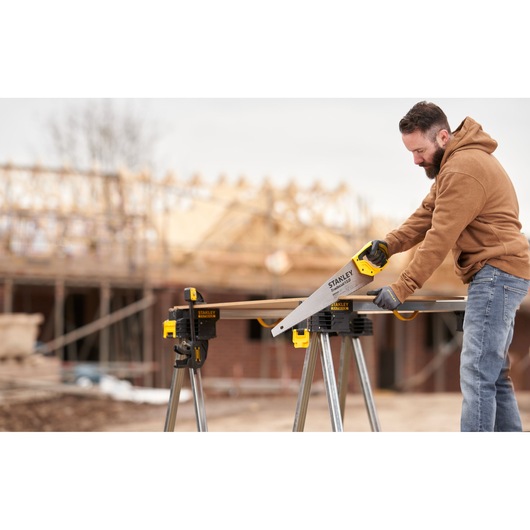STANLEY STHT1-20352 hand saw used outdoors on a construction site, cutting wood on a workbench.
