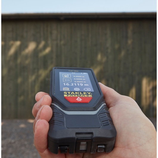 STANLEY STHT1-77142 laser distance measurer held in hand, outdoor use, display screen visible.