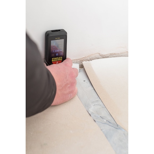 STANLEY STHT1-77142 laser distance measurer being used on a wall and floor corner.
