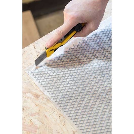 STANLEY STHT10268-0 utility knife cutting mesh on wood surface, close-up side angle.