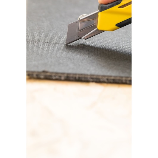 STANLEY STHT10270-0 utility knife cutting black material, close-up angle, yellow and black handle.