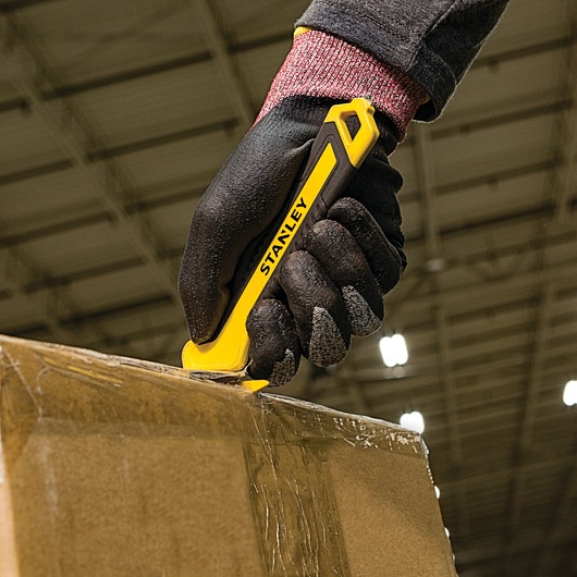 Stanley STHT10356 utility knife used to cut tape on a cardboard box, close-up, photo of product in use.