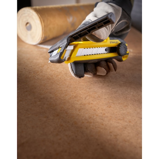 Photo of STANLEY STHT10500-0 utility knife in a gloved hand, yellow and black, on a work surface.