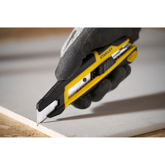 Photo of STANLEY STHT10500-0 utility knife with yellow and black body cutting drywall, held in gloved hand.