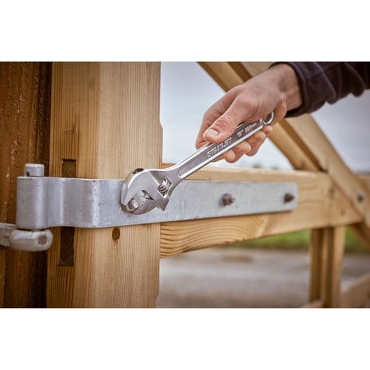 STANLEY STHT13122-0 adjustable wrench tightening a metal bolt on a wooden gate in outdoor setting.