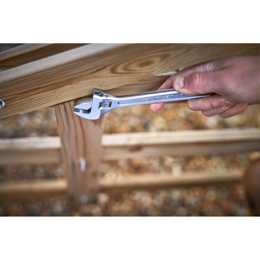 STANLEY STHT13122-0 adjustable wrench held to bolt on wooden structure, close-up photography.