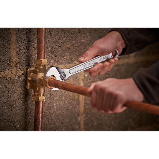 Photo of STANLEY STHT13123-0 adjustable wrench used on copper pipe near wall, tool held by hand.