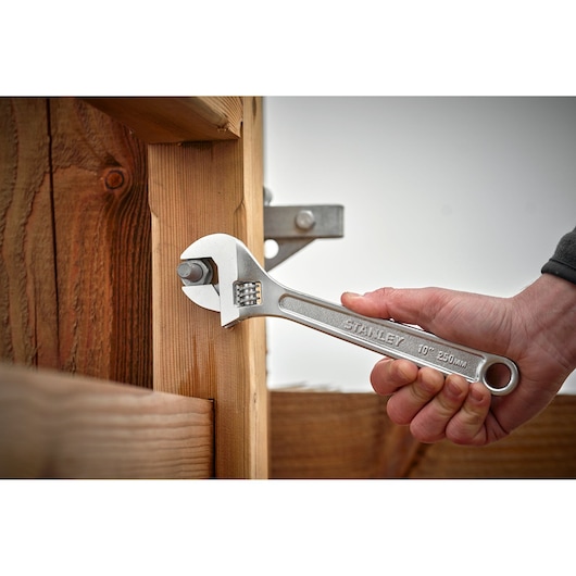 STANLEY STHT13156-0 adjustable wrench tightening a bolt on wooden structure, close-up photography.
