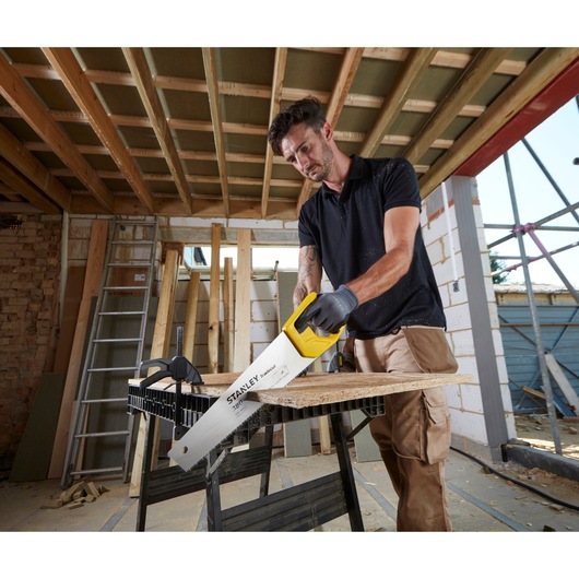 STANLEY STHT20348-1 hand saw with yellow handle cutting wood plank on construction site.