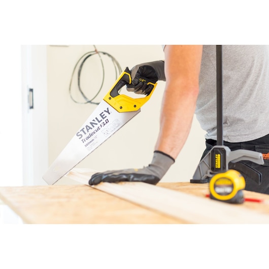STANLEY STHT20349-1 hand saw with yellow handle cutting wood, close-up in workshop setting.