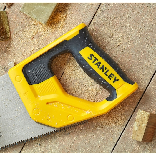 STANLEY STHT20354-1 handsaw with yellow and black handle, top view, lying on wooden surface with sawdust.
