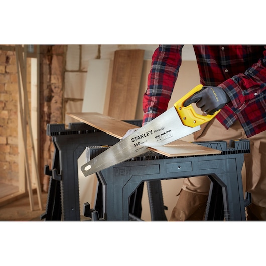 STANLEY STHT20370-1 hand saw with yellow handle cutting wood, photography of product in workshop setting.