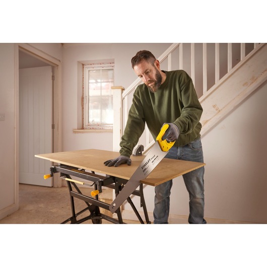 Stanley STHT20371-1 hand saw with yellow handle used for cutting wood on a workbench indoors.