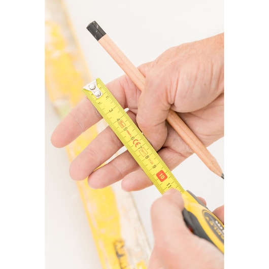 STANLEY STHT36803-0 tape measure with yellow blade and black case, close-up handheld shot with pencil.