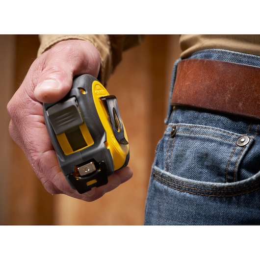 Photo of STANLEY STHT37232 tape measure held in hand next to jeans and brown leather belt.