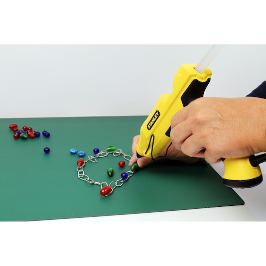 STANLEY STHT6-70417 glue gun in use attaching colorful beads to a metal chain, side angle.