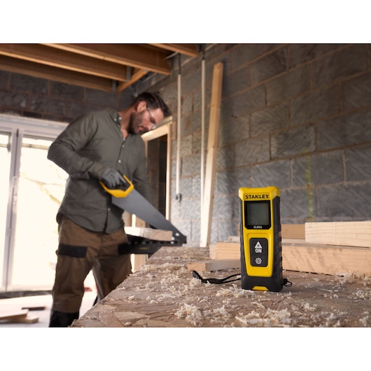 STANLEY STHT77065-0 laser distance measurer on workbench in woodworking workshop, yellow and black design.