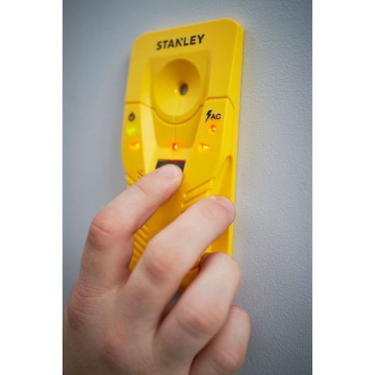 STANLEY STHT77587-0 stud finder tool yellow, front view, in use against a wall with LED indicators lit